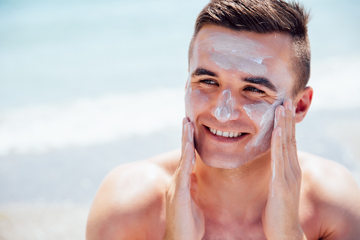 Cheerful Man Puts The Lotion On Face To Protect A Skin, On The Beach