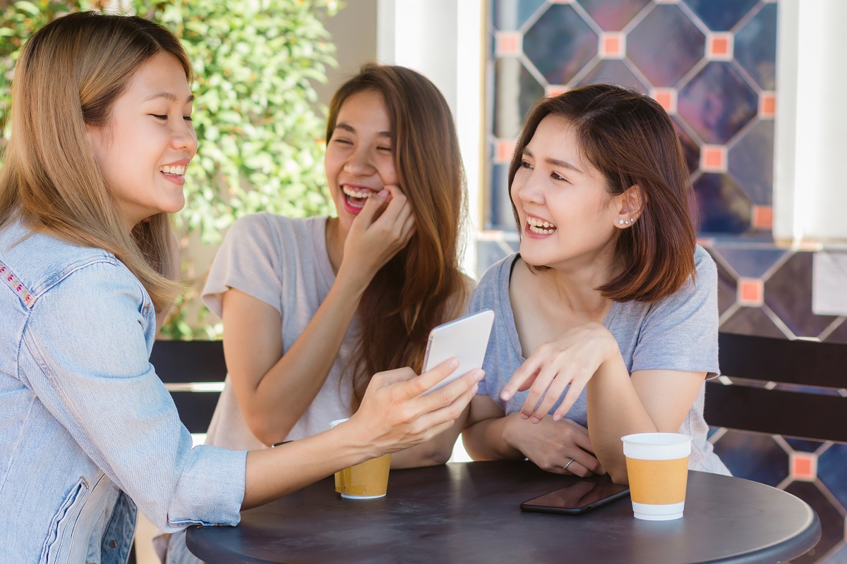 Cheerful Asian Young Women Sitting In Cafe Drinking Coffee With